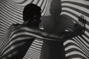 Man faces his own shadow against wall with curved lines