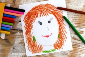 Child's drawing of mum, smiling with brown hair, next to pack of pens