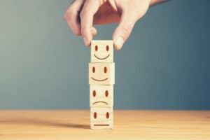Stack of four dice, showing sad, neutral, satisfied, and very satisfied expressions, with hand picking up the very satisfied dice